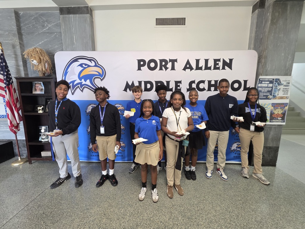Nine students in uniform pose in front of a Port Allen Middle School banner, next to an American flag.