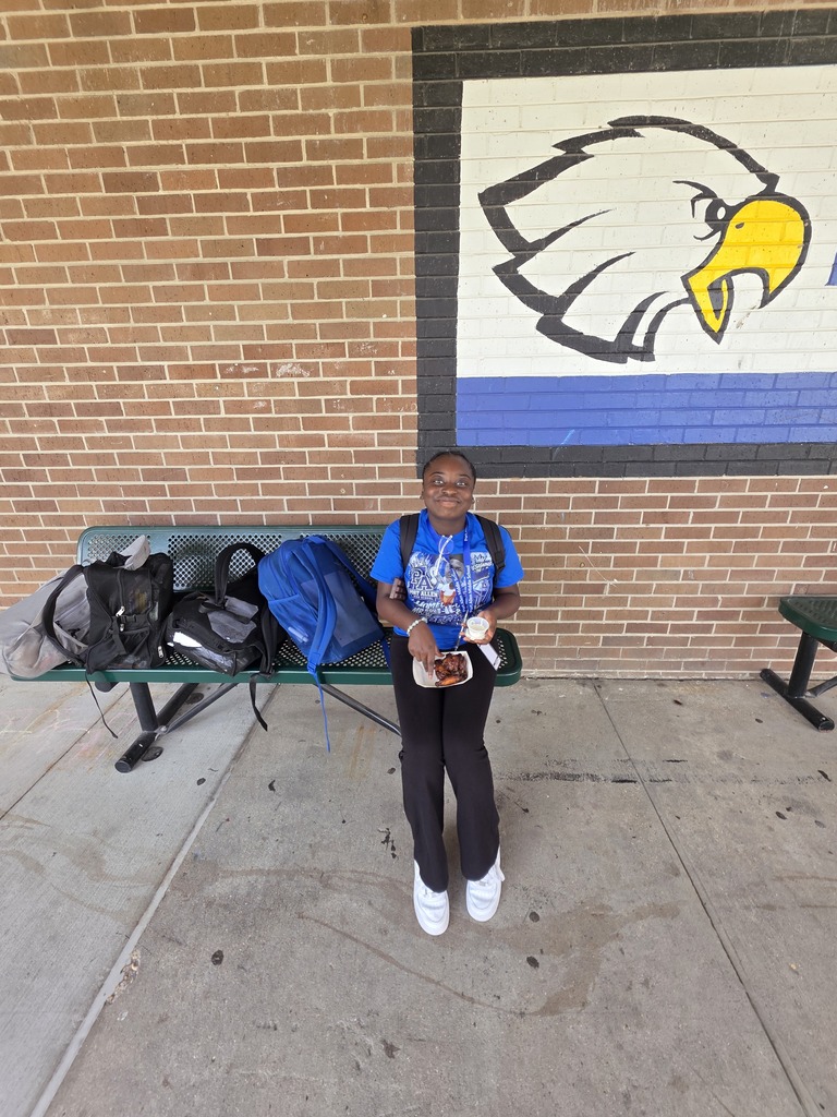 A person stands near a bench with bags on it, in front of a brick wall with an eagle mural.