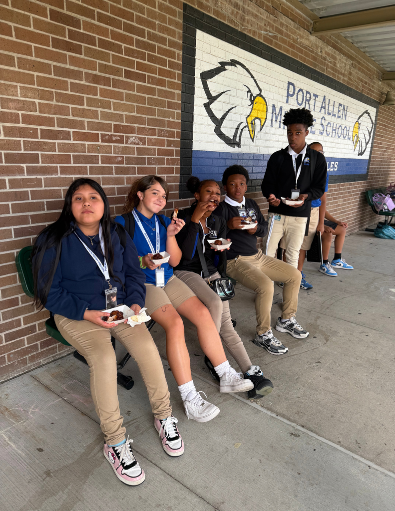 Several students sit on a brick wall, eating food. A sign for Port Allen Middle School is visible.