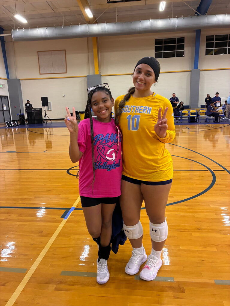 Two women, one in a yellow jersey, pose for a photo on a court. One makes a peace sign.