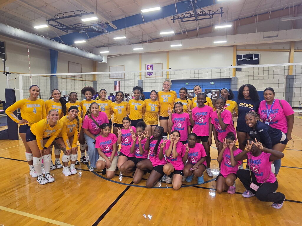 A group of women in yellow and pink jerseys, standing in a circle on a court.