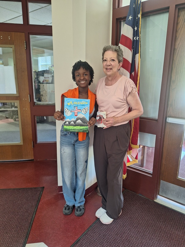 A pretty black girl with short braids and a bright orange shirt hold up her artwork - mountains and a blue sky with an eagle flying overhead.  She stands next to a VFW representative  - a woman with short gray hair - who is holding a gift card.  