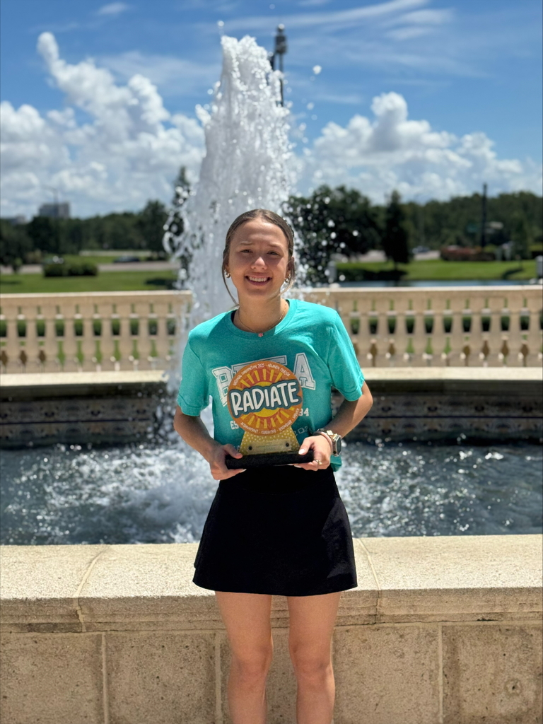 WCSSDS student with national beta trophy won during natiobnal competion, wearing beta shirt in front of a fountain
