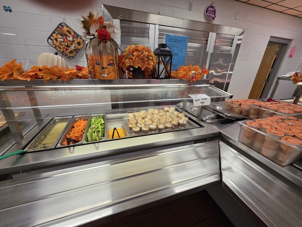 Decorated Cafeteria with orange leaves, pumpkins. Lunch line with themed offerings for Halloween including Witches’ Brew Chili, Gouled Cheese Sandwiches, Witch Finger carrot and celery sticks, and Spooky Pudding Cups!
