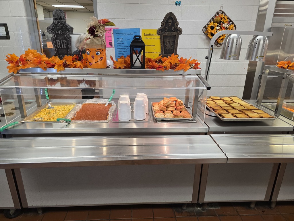 Decorated Cafeteria with orange leaves, pumpkins. Lunch line with themed offerings for Halloween including Witches’ Brew Chili, Gouled Cheese Sandwiches, Witch Finger carrot and celery sticks, and Spooky Pudding Cups!