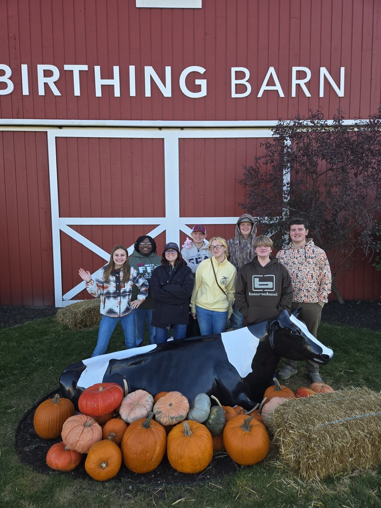 West Carroll FFA students posed in front of a birthing barn. Featuring a cow figurine and pumpkin display.