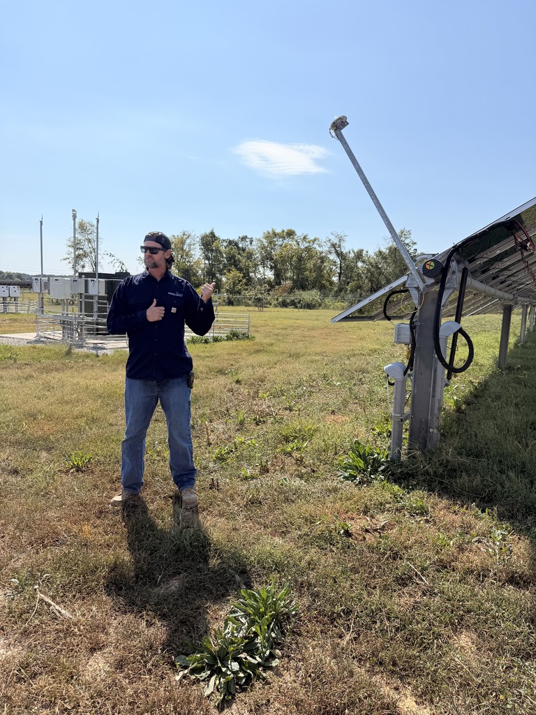 A Silicon Ranch representative explains solar farm equipment during a tour of the Trezevant Solar Farm, with solar panels and electrical equipment visible nearby.