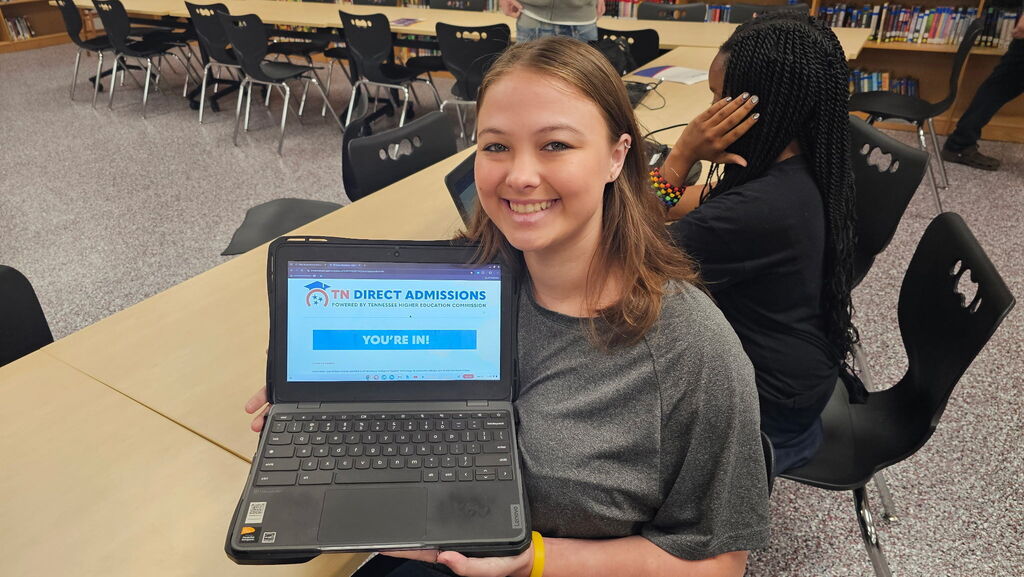 A smiling West Carroll senior holds up her laptop displaying the TN Direct Admissions website with a large “YOU’RE IN!” message after receiving a direct admission offer.