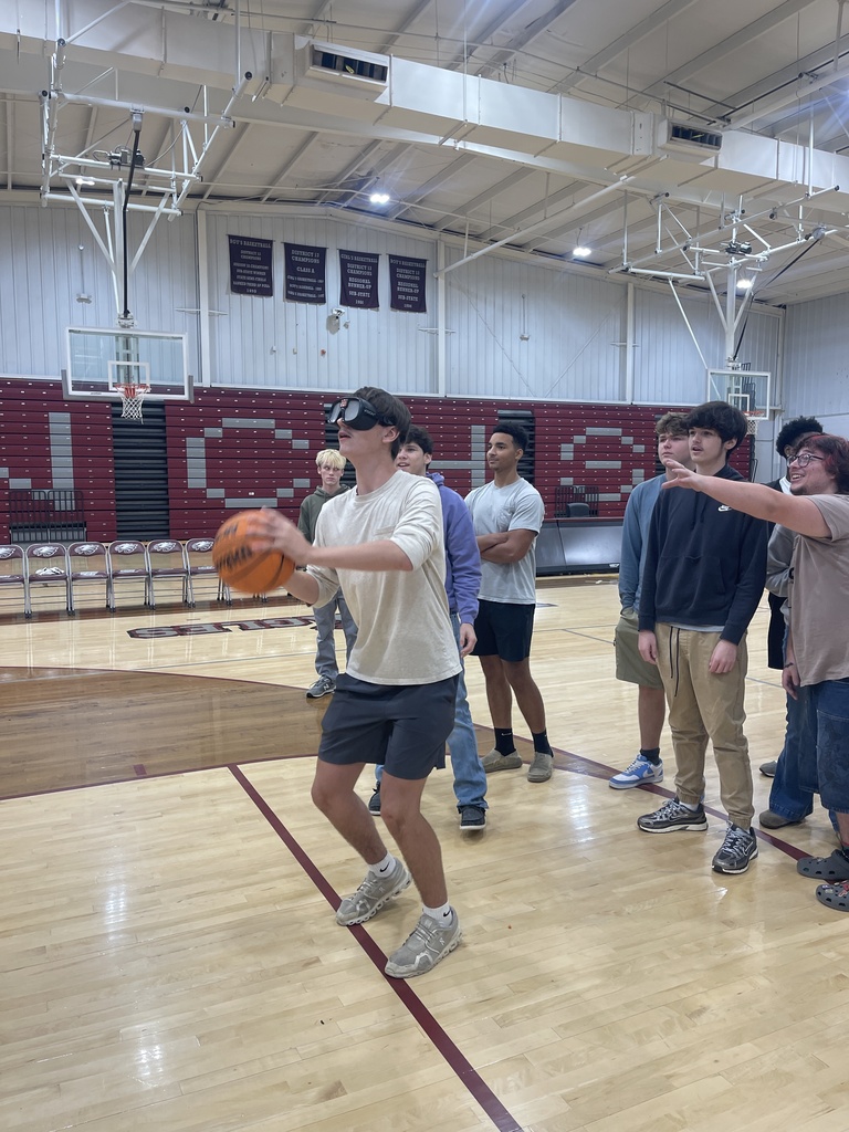 A West Carroll student attempts to handle a basketball while wearing impairment-simulation goggles as classmates watch during the Choices Matter program.