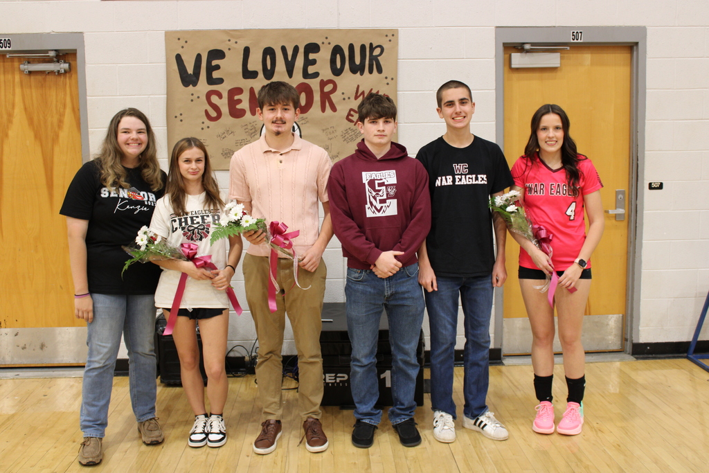 West Carroll senior athletes from volleyball, golf, and cross country gather together during Senior Night, several holding flowers presented during the recognition.