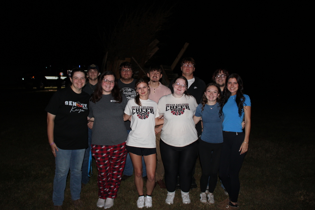 Series of photos from the West Carroll Homecoming Bonfire held at night on school grounds. Students and staff gather with friends around a large bonfire, pose for group photos, and enjoy the Homecoming celebration. West Carroll cheerleaders perform near the fire and serve refreshments, while additional photos show the bonfire being prepared and lit with safety personnel nearby.