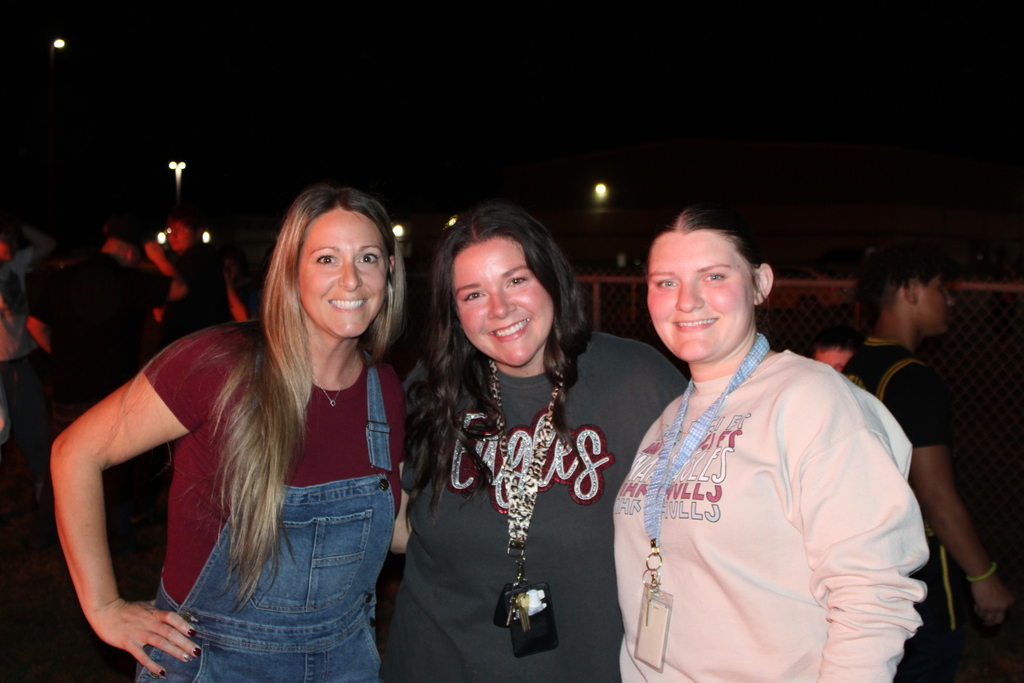 Series of photos from the West Carroll Homecoming Bonfire held at night on school grounds. Students and staff gather with friends around a large bonfire, pose for group photos, and enjoy the Homecoming celebration. West Carroll cheerleaders perform near the fire and serve refreshments, while additional photos show the bonfire being prepared and lit with safety personnel nearby.