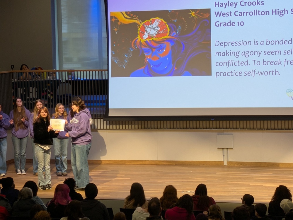 Girl getting award in front of a drop down screen with artwork