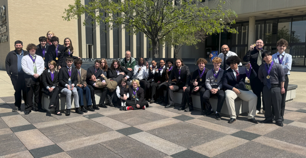group of students and staff in business attire posing outside with a tree and building behind them