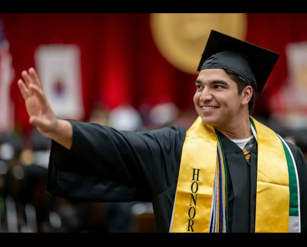 Boy in black cap and gown with an honors scarf