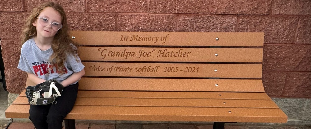 Girl sitting on a bench with a baseball glove. The bench says In Memory of Grandpa Joe Hatcher.
