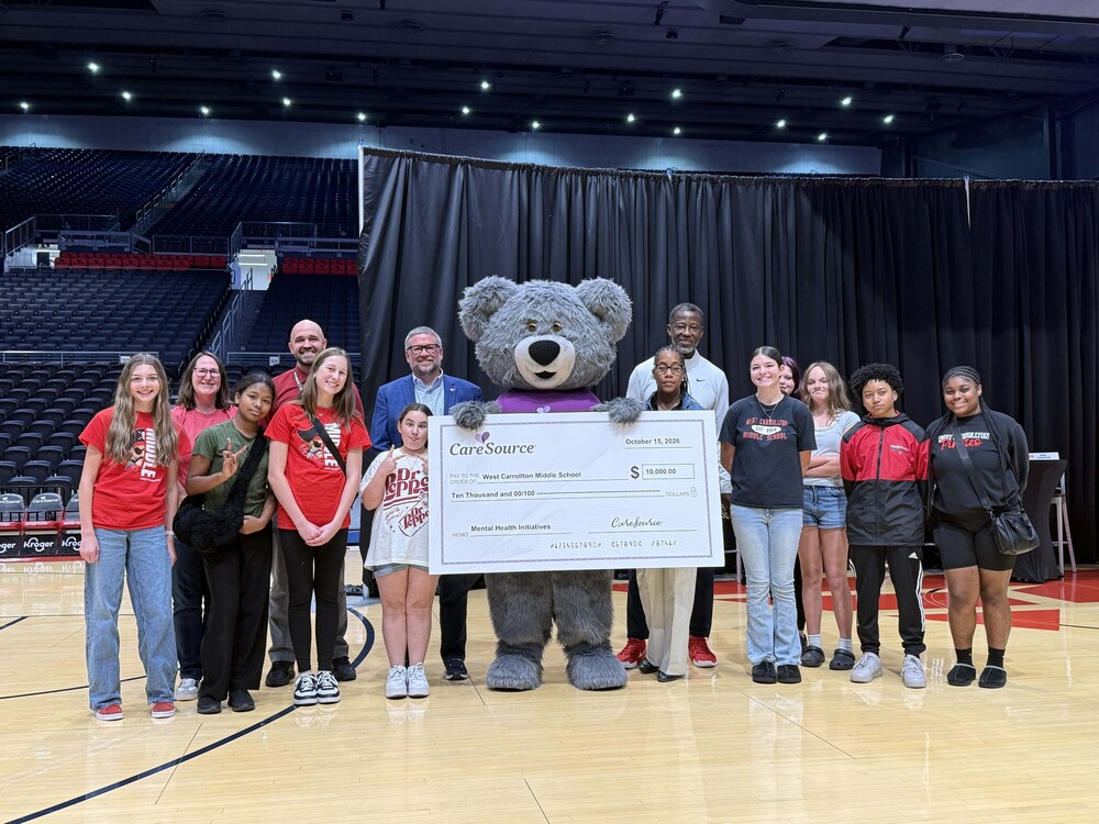 Goup of people gather around a bear mascot who is holding a check from Care Source for $10,000