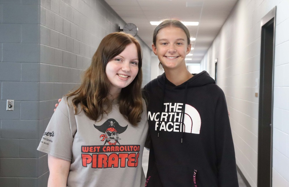 two girls standing in a school hallway, one with a West Carrollton Pirate tshirt and the other with a The North Face hoodie