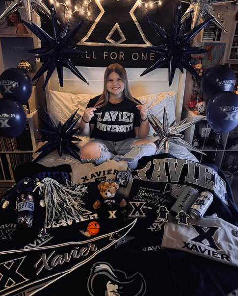 Girl smiling wearing a shirt that says Xavier University surrounded by Xavier items