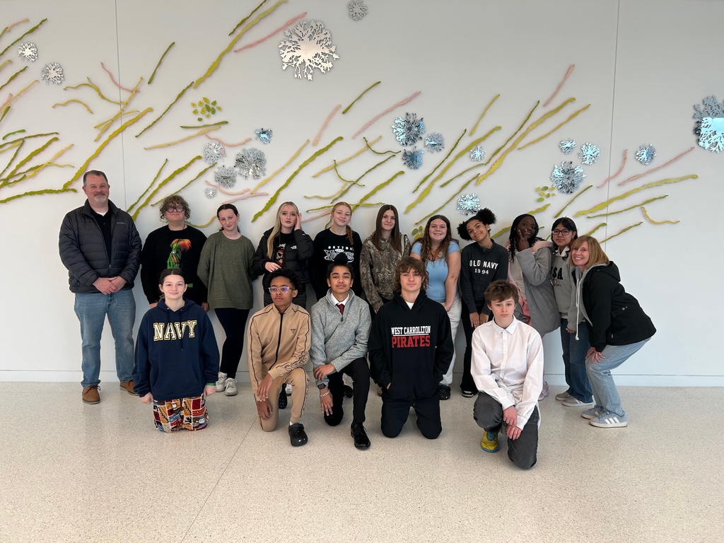 students posing in front of wall with sculpture art