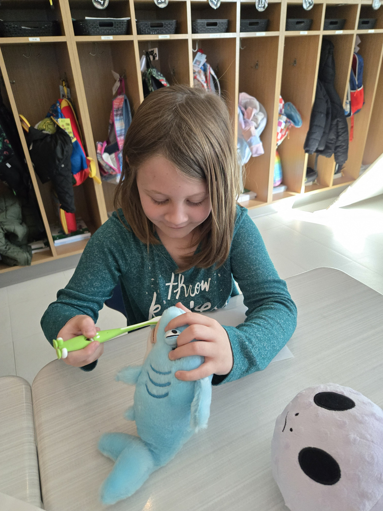 girl brushing teeth of a stuffed animal