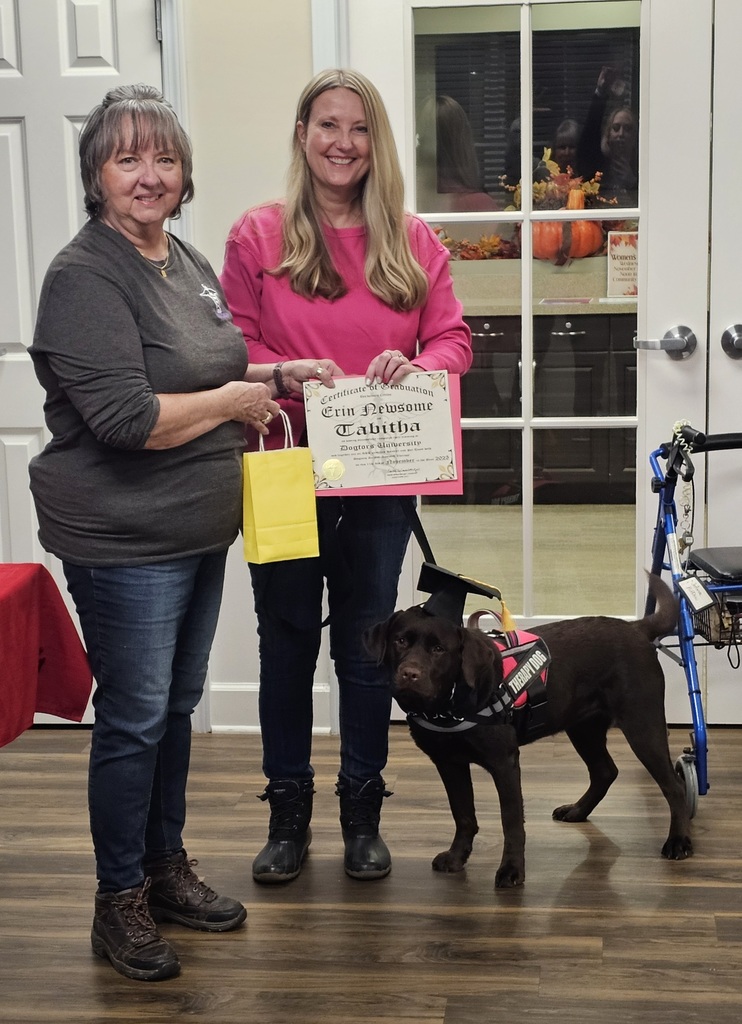 Two women with a dog. One is holding a  certificate of graduation.