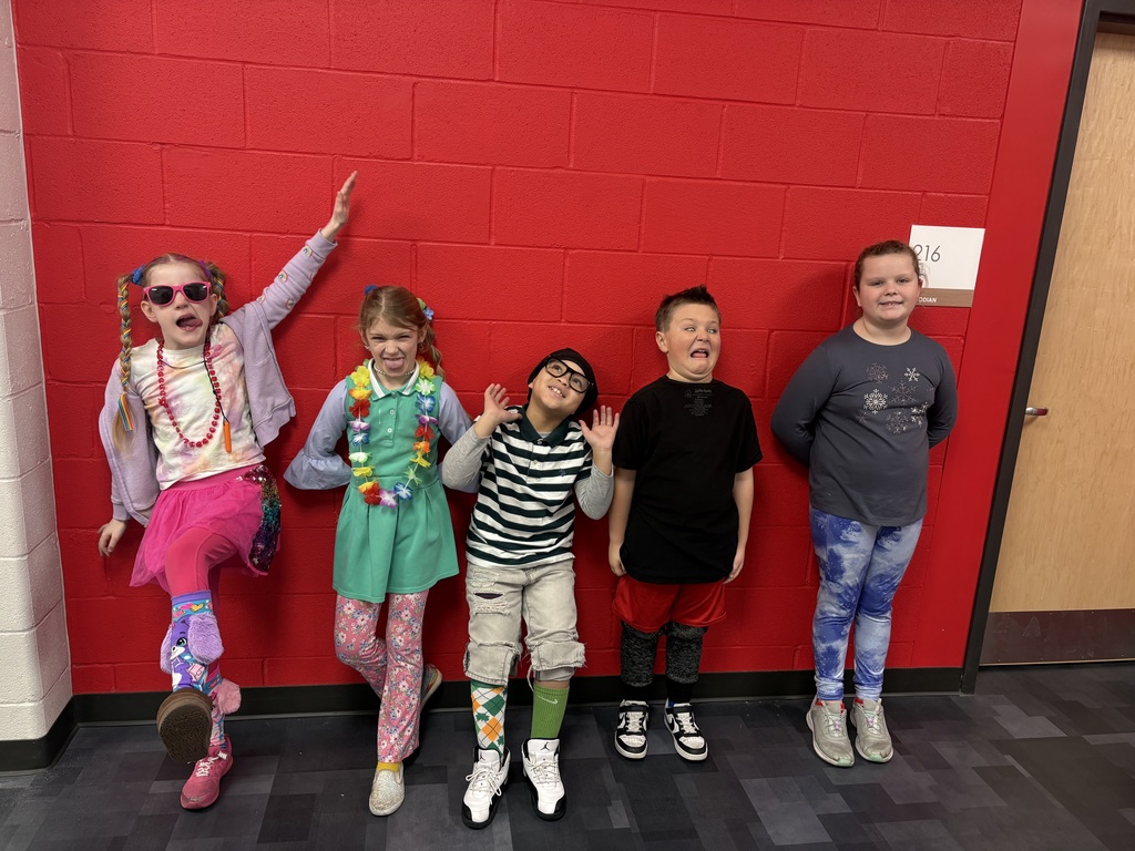 Five students wearing wacky clothes and doing wacky poses in front of a red background