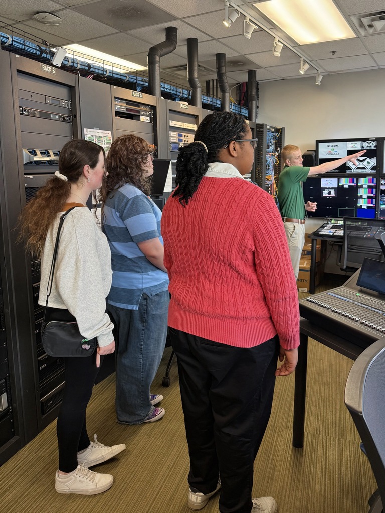 3 students in a control room with a man pointing