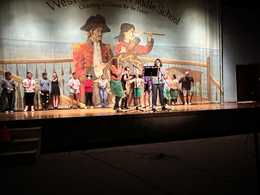 two teachers on stage with students lined up behind them