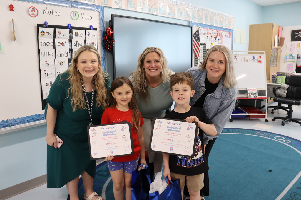 Five people stand in a classroom, three women and two children. They hold certificates and smile.