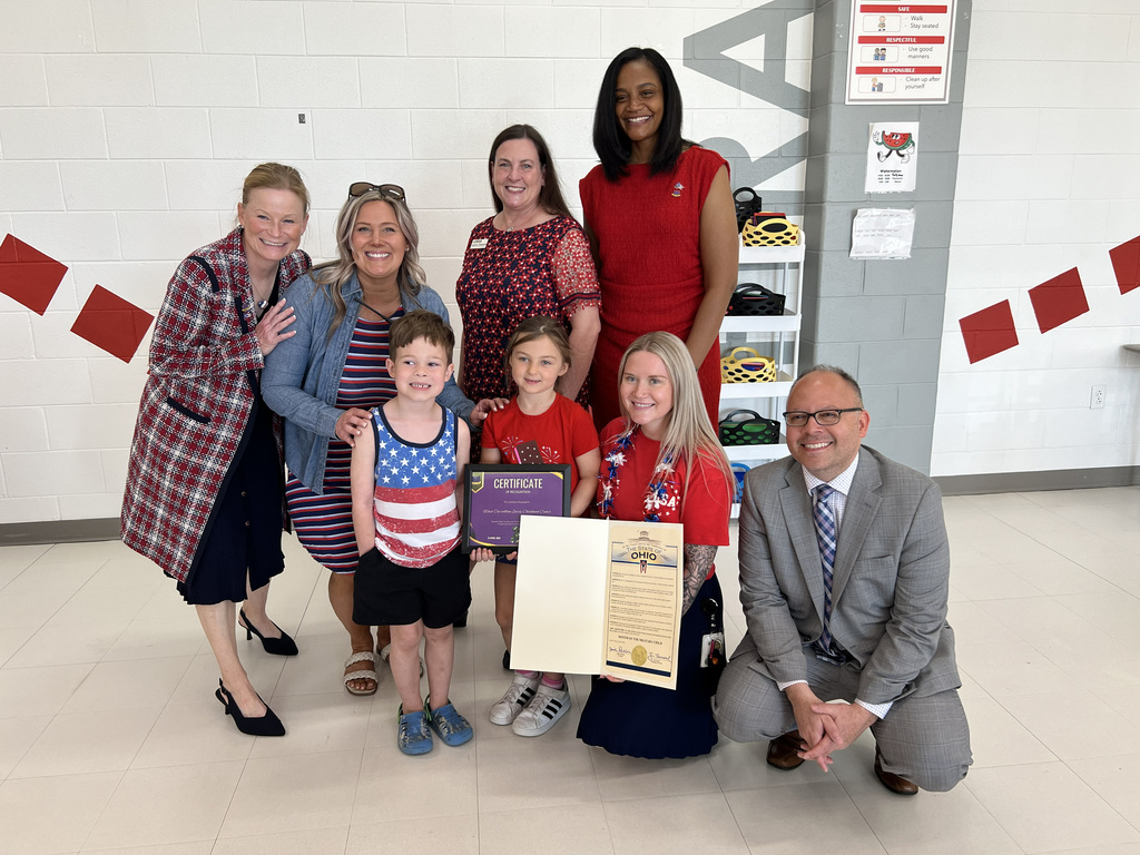 A group of adults and children in formal attire pose together, smiling, with two children holding certificates.