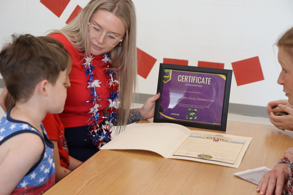 Woman holding a framed certificate shows it to two children. One child is looking at the certificate.