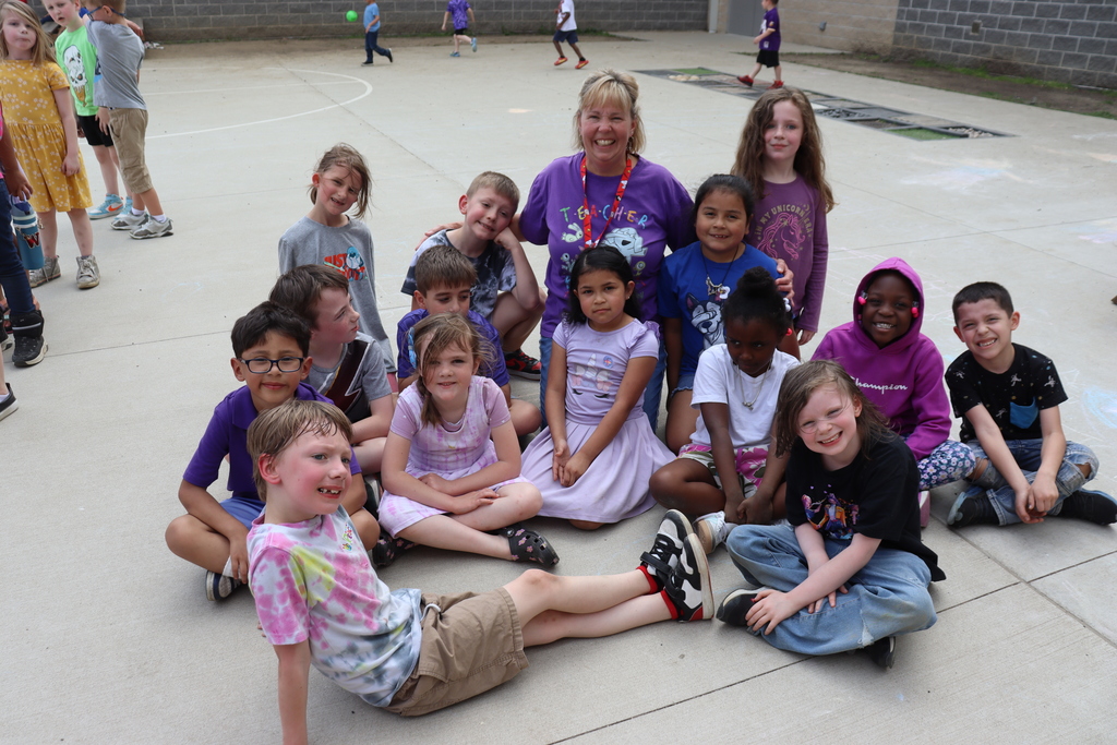 A group of children sitting in a circle on a paved playground with a woman.