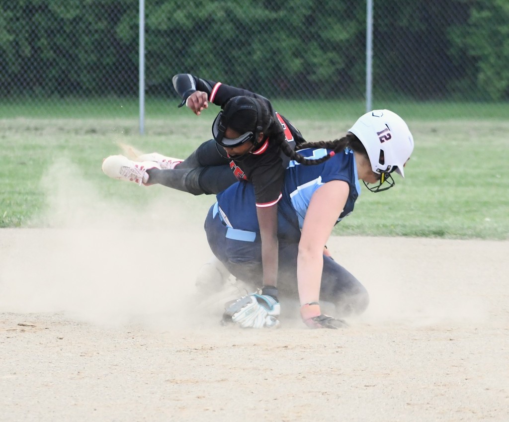 Two women playing softball. One is sliding into base while the other is on the ground, both wearing helmets.