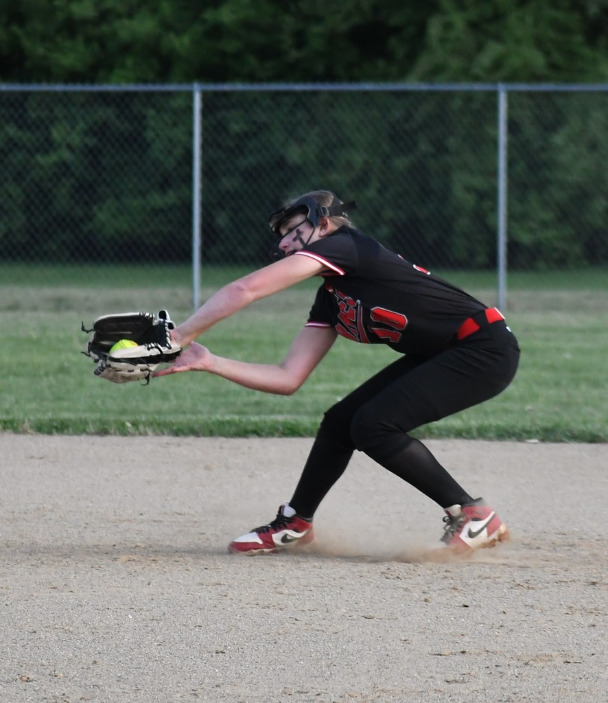 A female player in a black uniform is catching a ball while sliding on a dirt field.