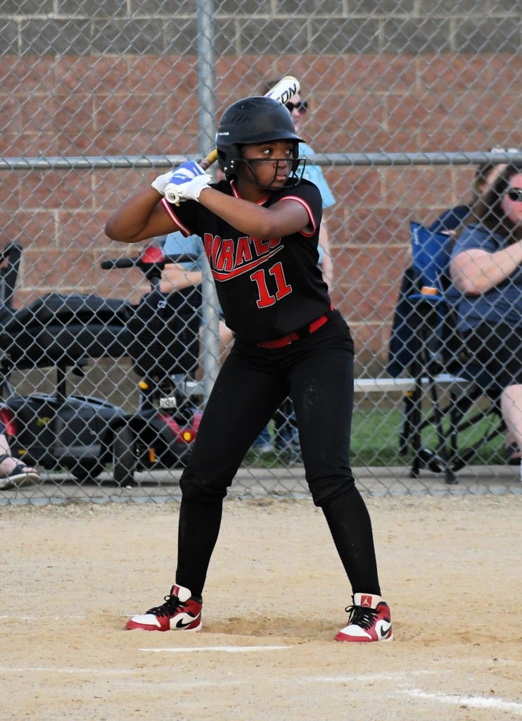 Player with number 11 in black uniform at bat, fence and seated people in background.
