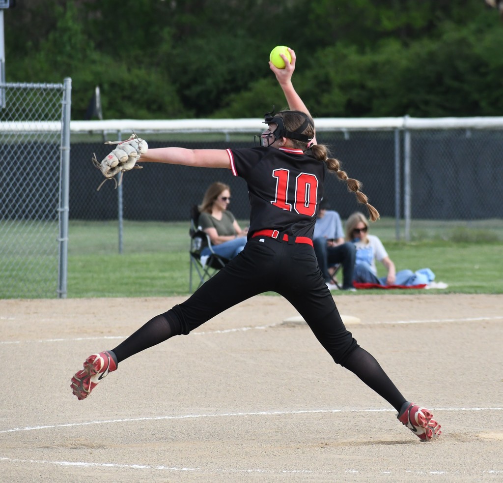 Player with jersey number 10 in a pitch position on a baseball field. Two people sitting on lawn chairs are watching.