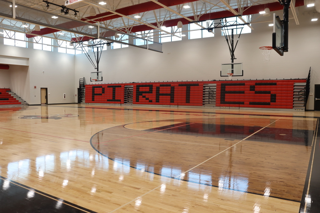 An indoor basketball court with red and white bleachers in the background. The court is empty.