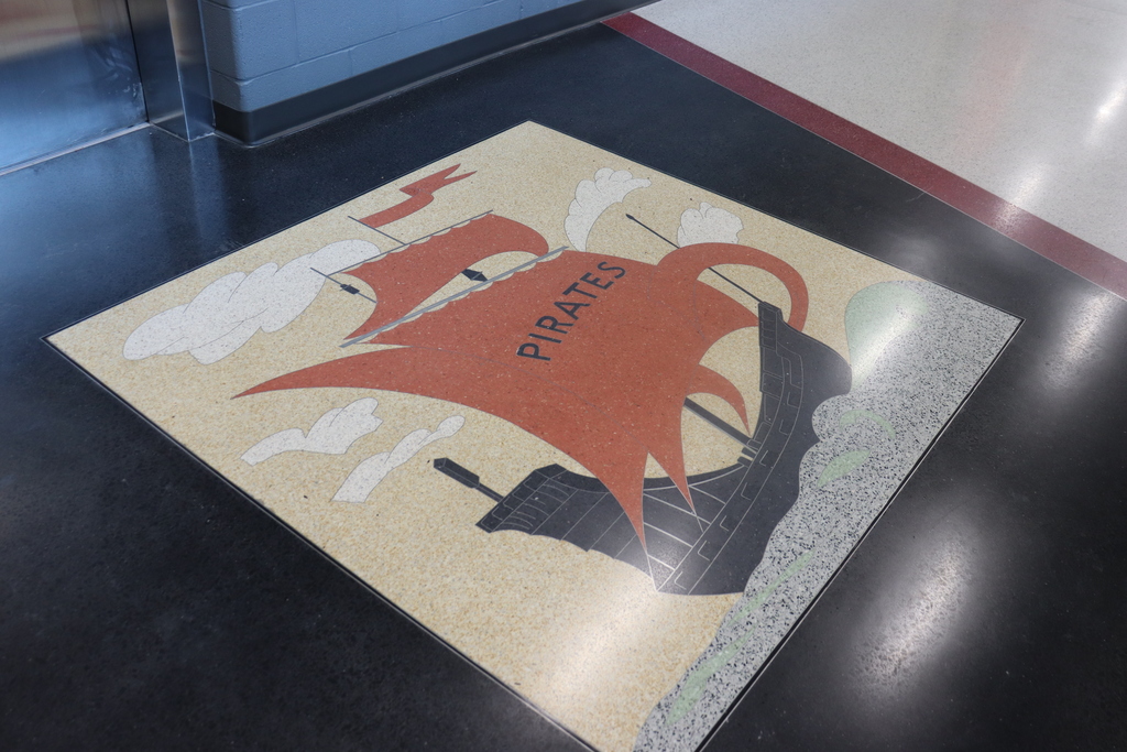 A square floor design features a pirate ship with a red sail and the word "Pirates". It is placed on a black floor with white and red borders.