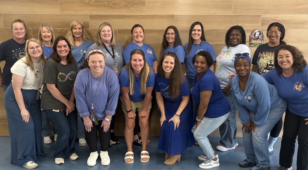A group of people wearing matching blue shirts stands in front of a wooden wall, smiling for a photograph.