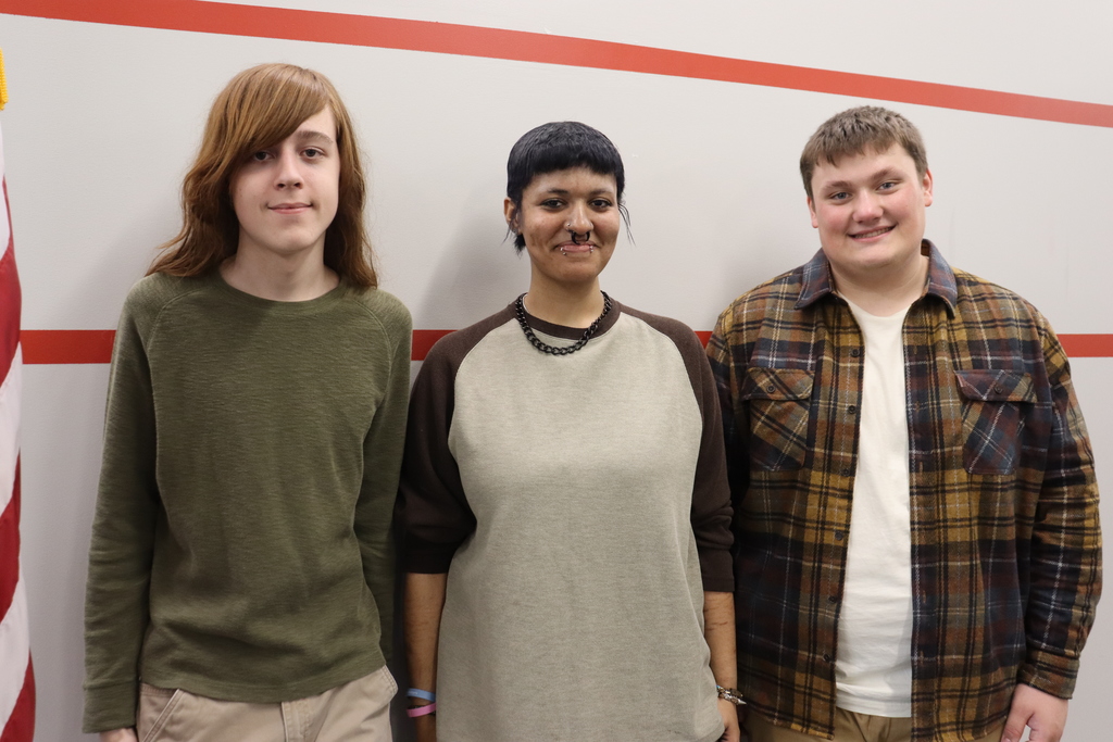 Three people standing together in front of a wall with red and white stripes.