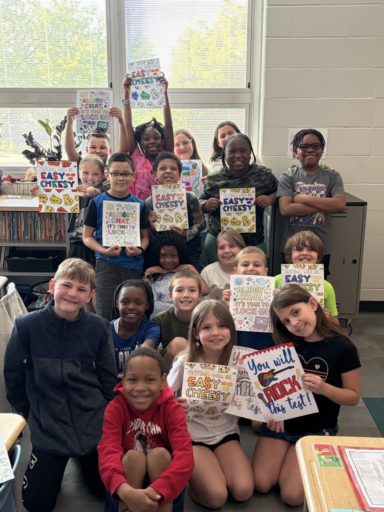 A group of students, some standing and some sitting, are holding up signs in a classroom.
