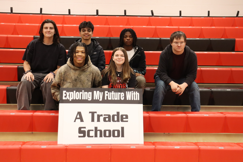 Six individuals pose on a red bleacher, with a sign in front reading "Exploring My Future With A Trade School".