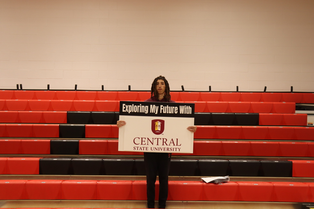 Person holding a sign for Central State University, standing in front of a row of red bleachers.