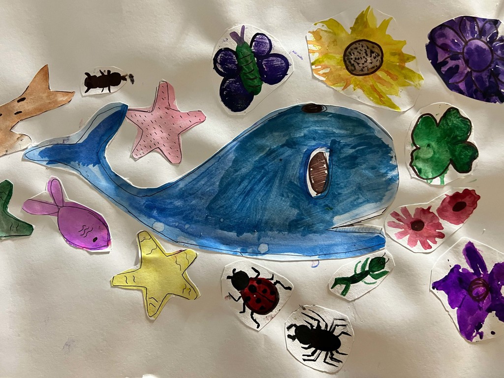 A large blue whale painting with a belly opening is surrounded by other hand-painted items. These include flowers, stars, and animals.