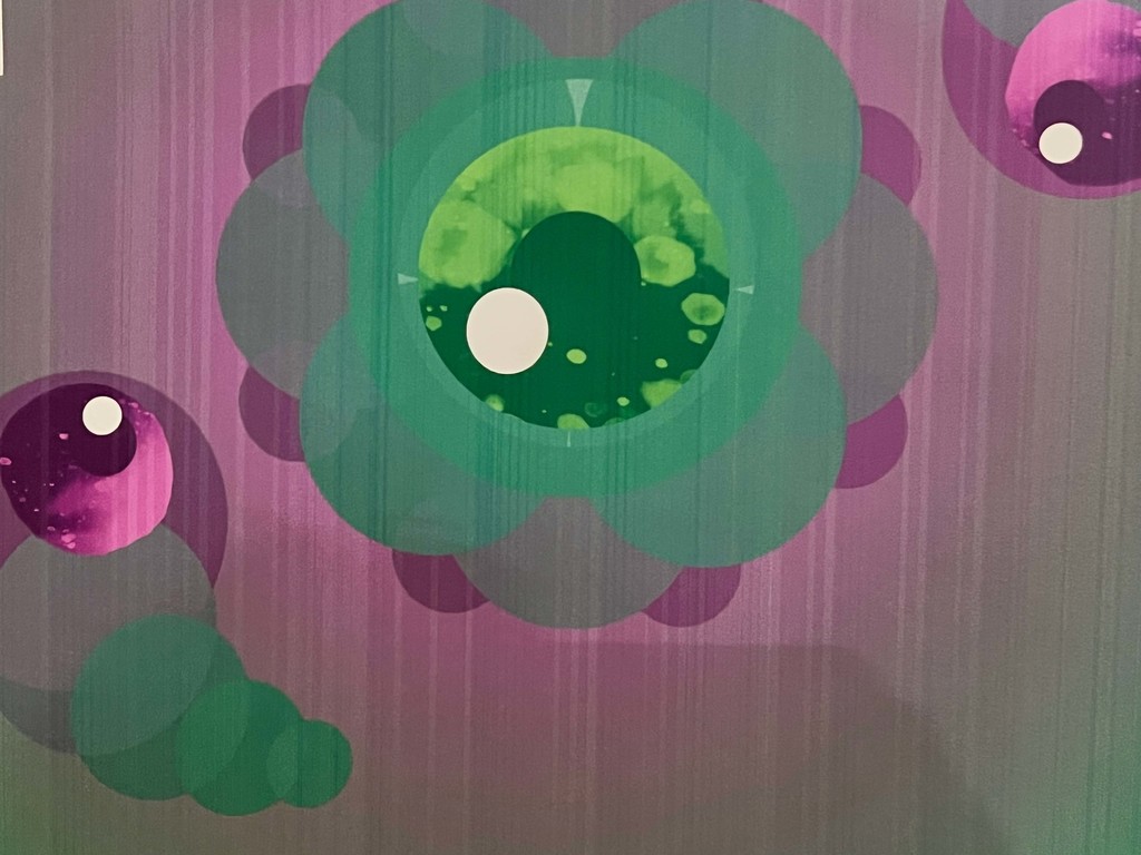 An abstract design featuring three circular forms. The largest one is a large green circle with a white dot in the center. The background is purple.