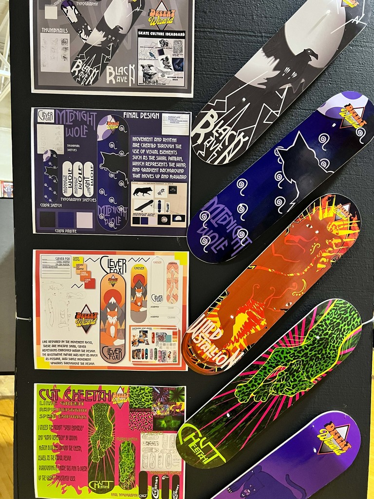 Display of skateboards with various designs on a black background, including blue, orange, green, and purple designs.