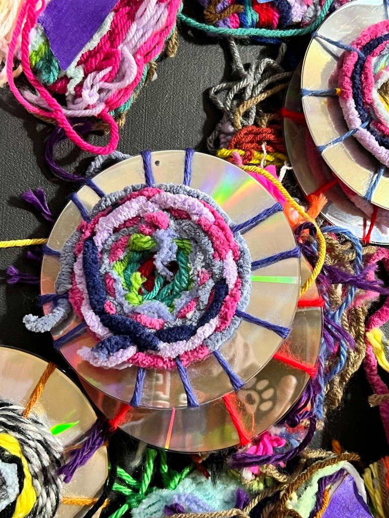 A collection of colorful circular items made of yarn on a table. The yarn is arranged in spirals and shapes.