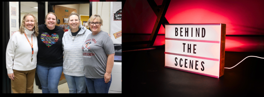 Four women pose for a photo inside a building. A light box reading "Behind the Scenes" is illuminated with red light.