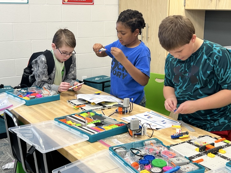 boys working together with colorful pieces to complete a robotic arm 